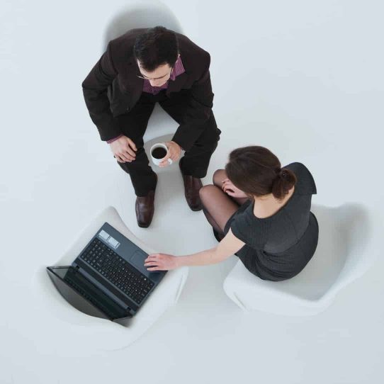 Overhead image of a man and woman dressed in black looking at a laptop while drinking black coffee